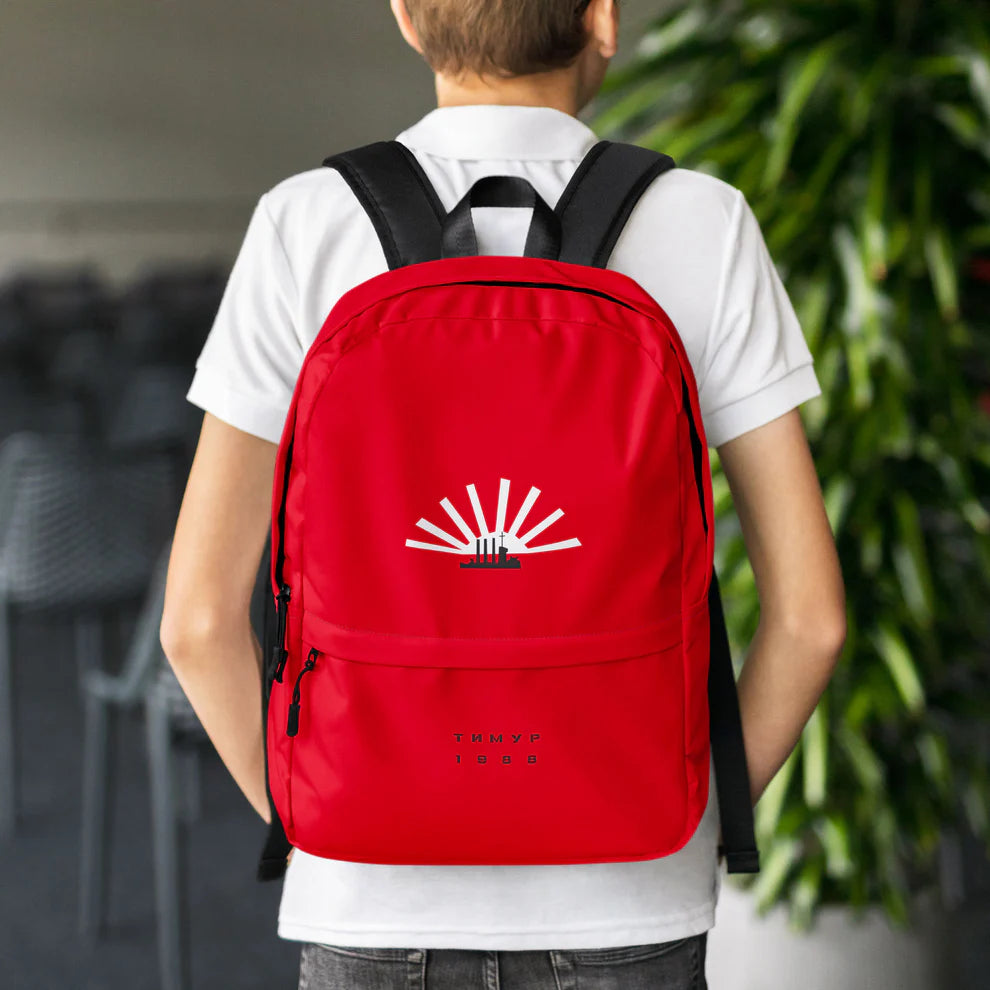 Young model teenage school boy wearing Timur Novikov backpack with “Aurora” artwork featuring the cruiser Aurora and a sun on a red background. www.timurnovikov.art
